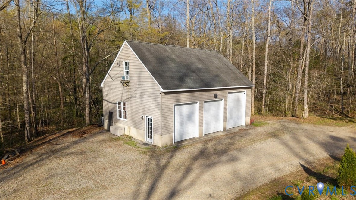 Detached three-bay structure featuring light-colored vinyl siding, a gable roof, concrete foundation, and an expansive gravel driveway