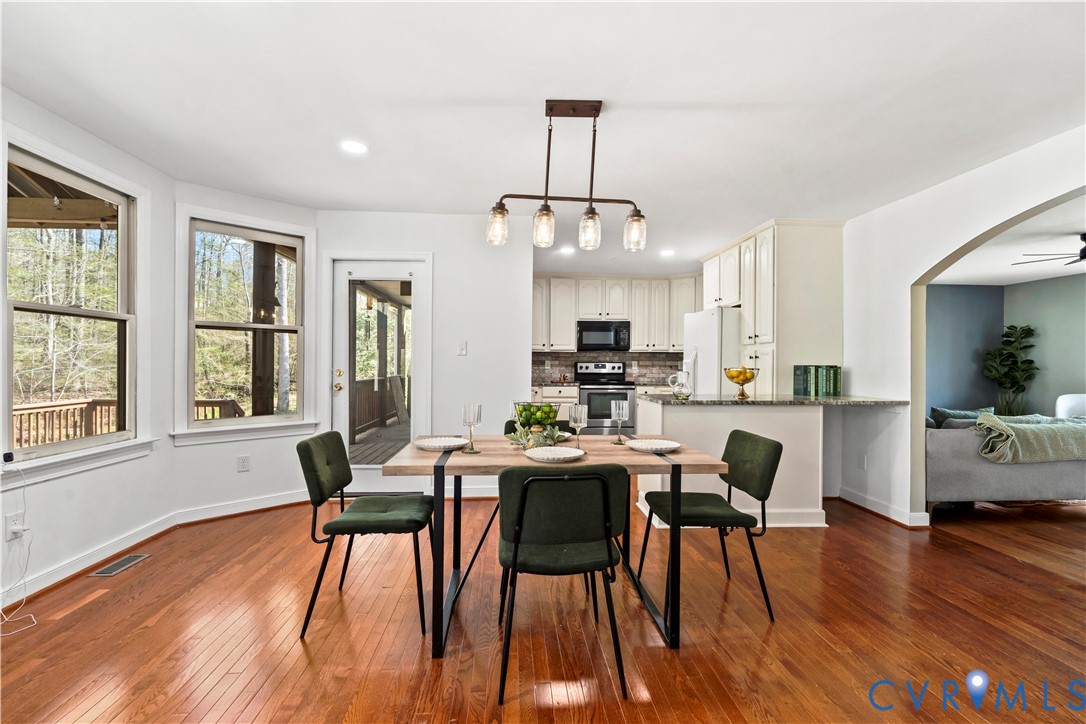 Dining area featuring wood-finish flooring, multi-light linear pendant fixture, oversized bay windows, and glass-paneled exterior door Dining area featuring wood-finish flooring, multi-light linear pendant fixture, oversized bay windows, and glass-paneled exterior door
