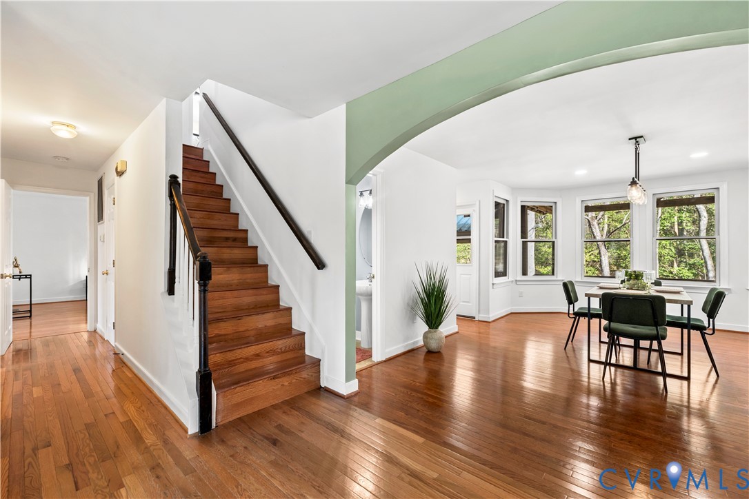 Open-concept interior featuring wood-finish flooring, a staircase with a black handrail and wood treads, an arched entryway, and multiple double-hung windows