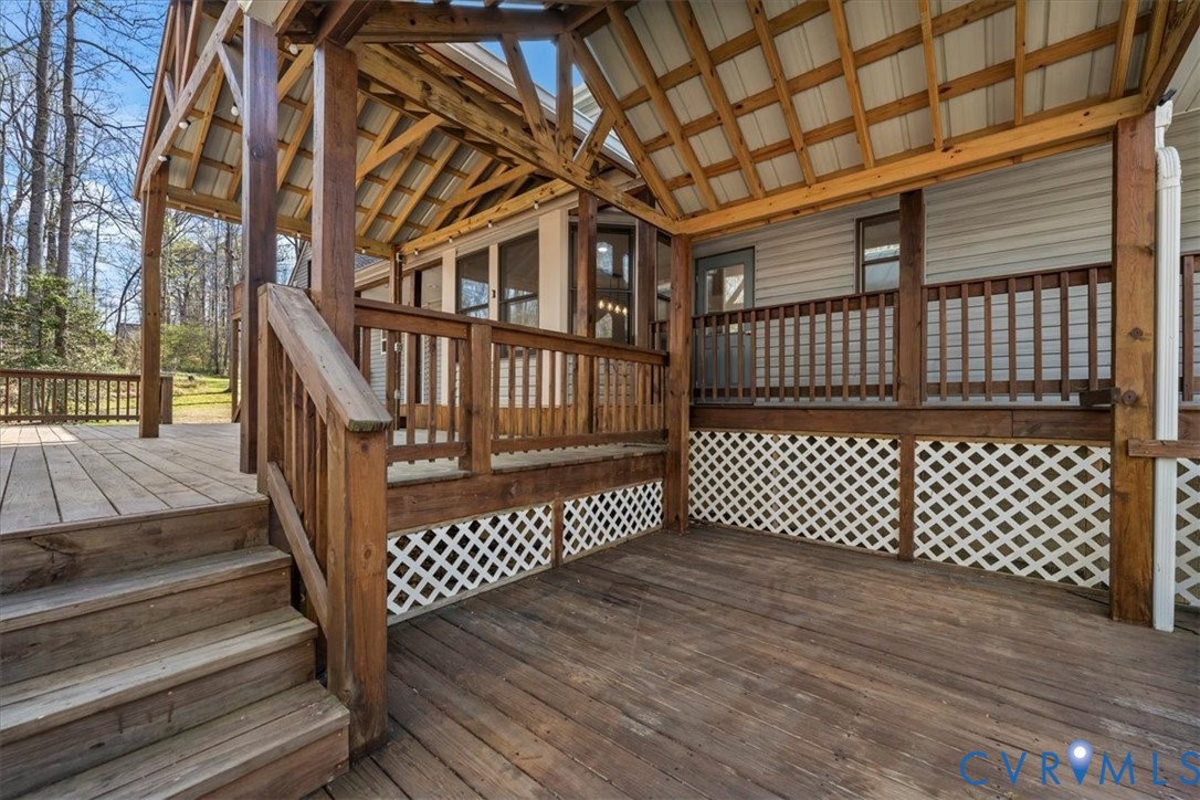 Multi-level wooden deck featuring a covered gable roof, exposed timber framing, wooden railings, and white lattice skirting