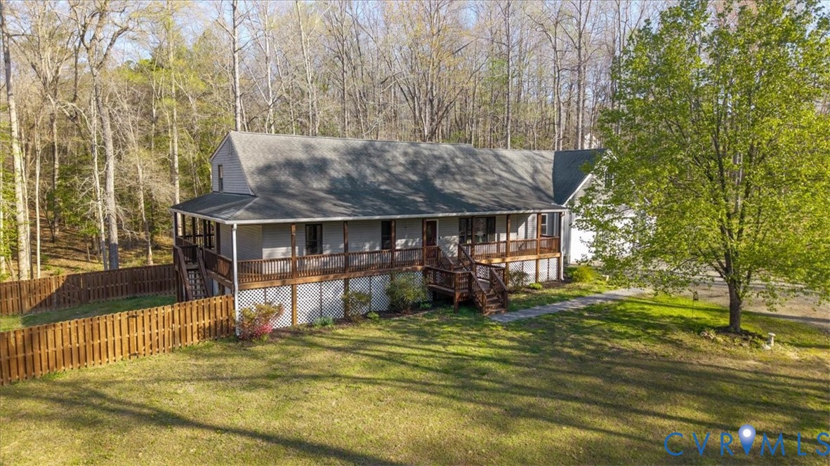 Two-story residence featuring grey siding, an elevated wrap-around wood deck, lattice skirting, a wood privacy fence, and a wooded lot