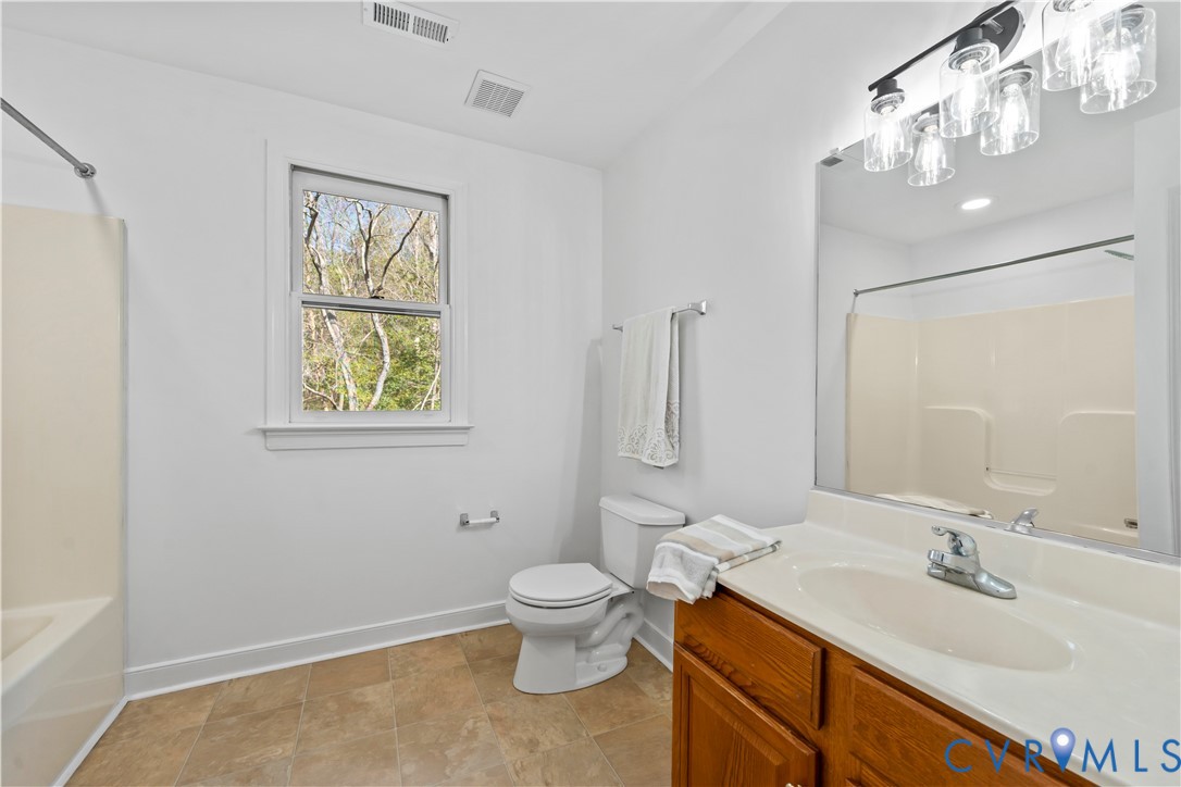 Full bathroom featuring a wood-finish vanity with an integrated basin, a large-format mirror, multi-light fixture, and tile flooring