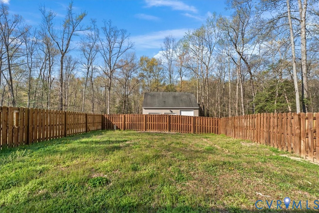 Fenced backyard featuring wood-panel fencing, grass lawn, and mature trees