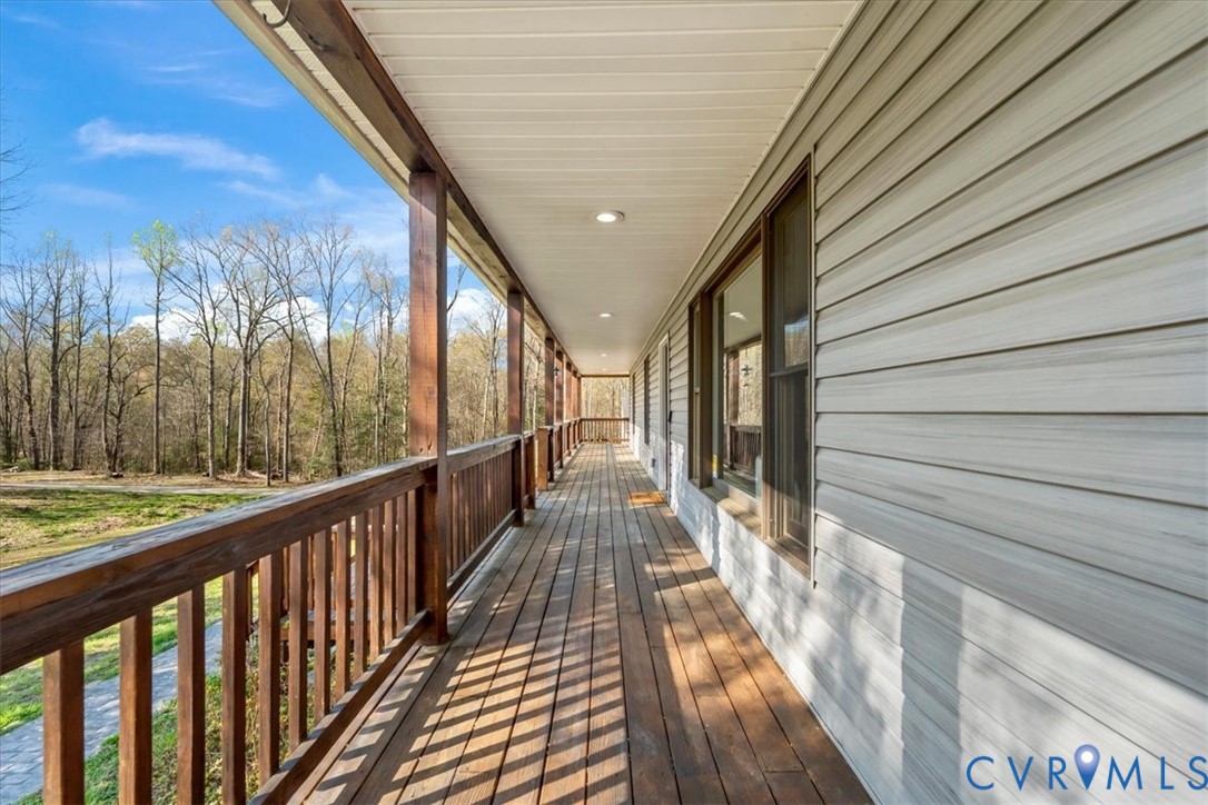 Covered wrap-around porch featuring wood-finish decking, stained wood railings, light-grey horizontal siding, and recessed ceiling lighting
