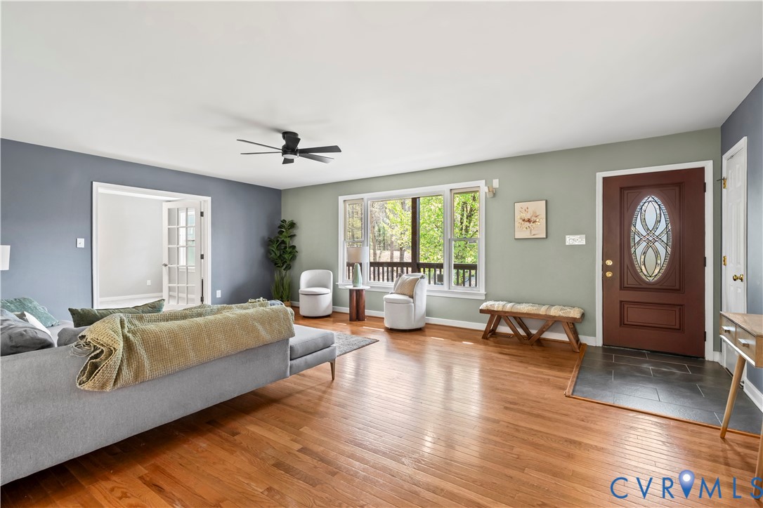 Wood-finish flooring, dark-toned tile entry, multi-pane glass entry door with decorative inlay, large multi-panel window, and matte black ceiling fan Wood-finish flooring, dark-toned tile entry, multi-pane glass entry door with decorative inlay, large multi-panel window, and matte black ceiling fan