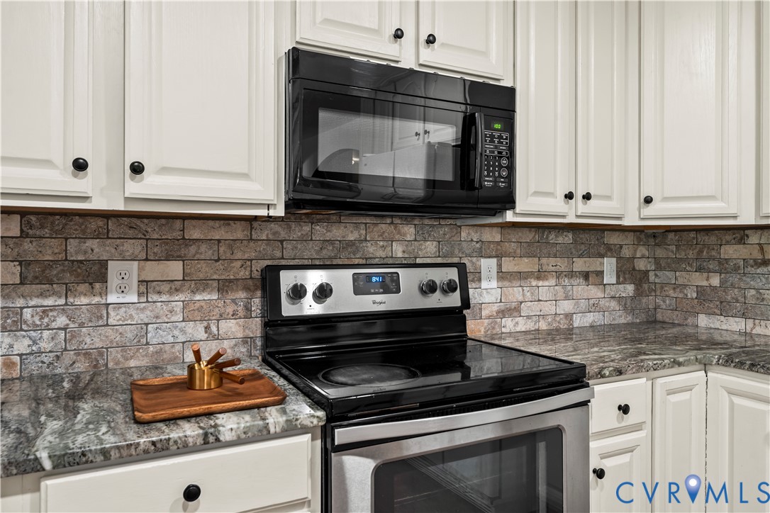 Kitchen featuring shaker-style cabinetry, stone-finish countertops, brick-style tile backsplash, and integrated black-finish appliances