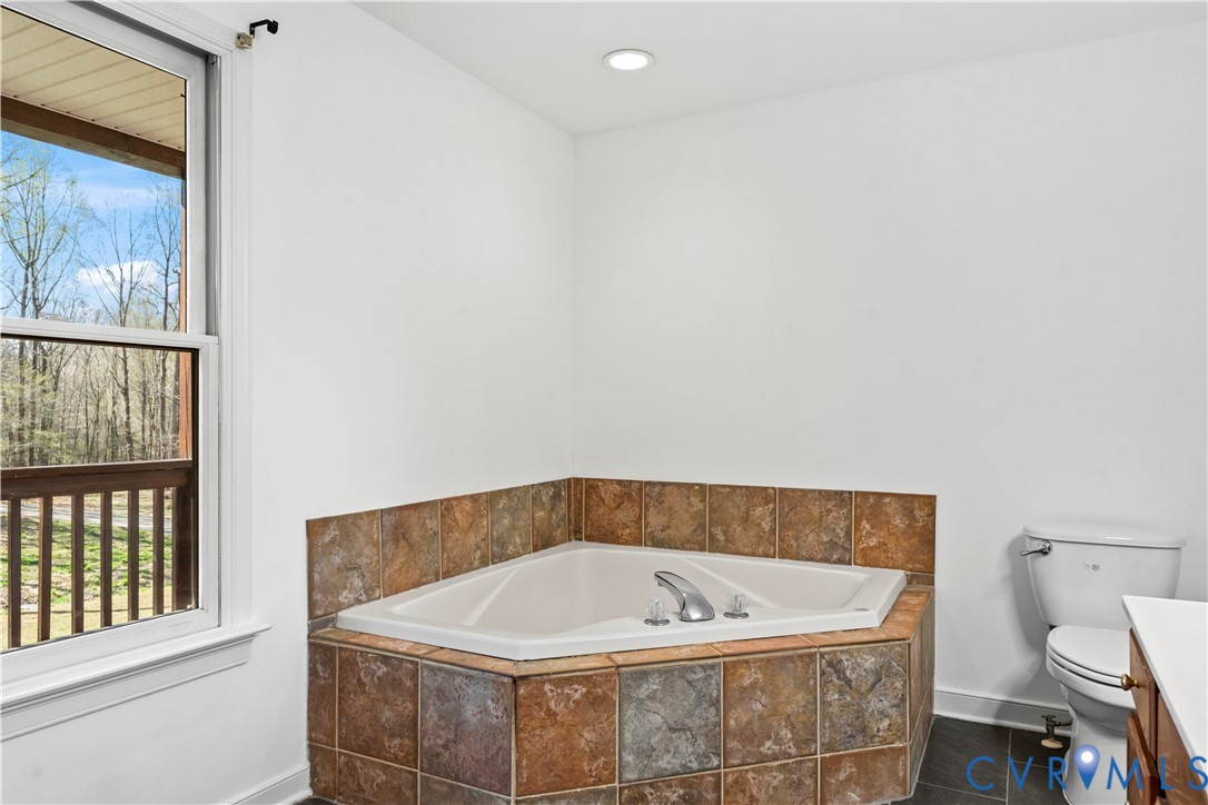 Corner soaking tub featuring a tile surround, chrome faucet fixtures, and a dual-pane window
