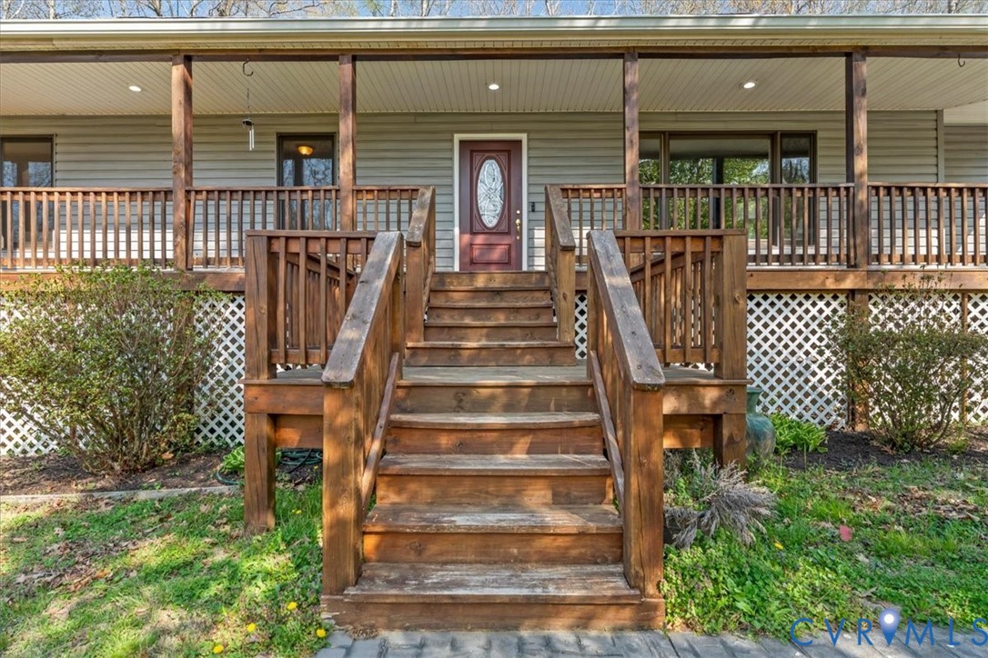 Covered front porch featuring a wooden staircase, horizontal siding, lattice skirting, and a door with an oval glass inset