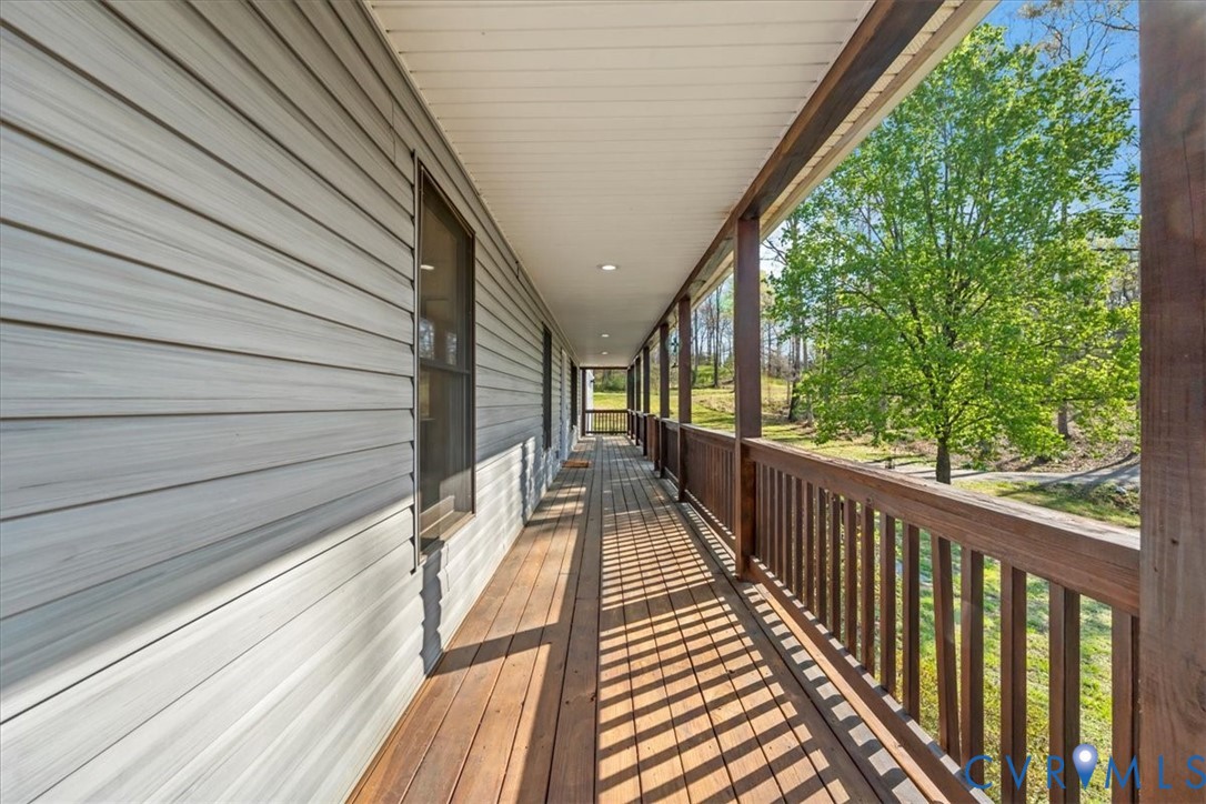 Covered wrap-around porch featuring wood-finish decking, dark-stained wood railings, recessed lighting, and horizontal siding