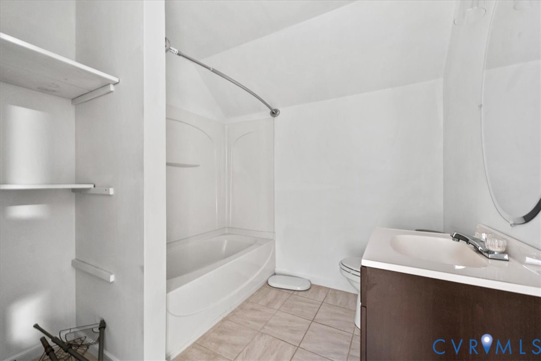 Bathroom featuring a dark wood-finish vanity with a light-toned countertop, integrated tub and shower combination with a curved rod, oval wall mirror, and tile flooring