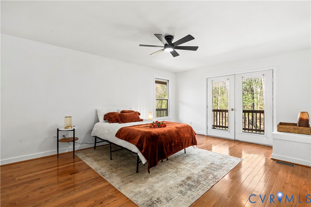 Room featuring wood-finish flooring, a matte black ceiling fan with integrated lighting, and glass-paned double doors opening to an exterior deck