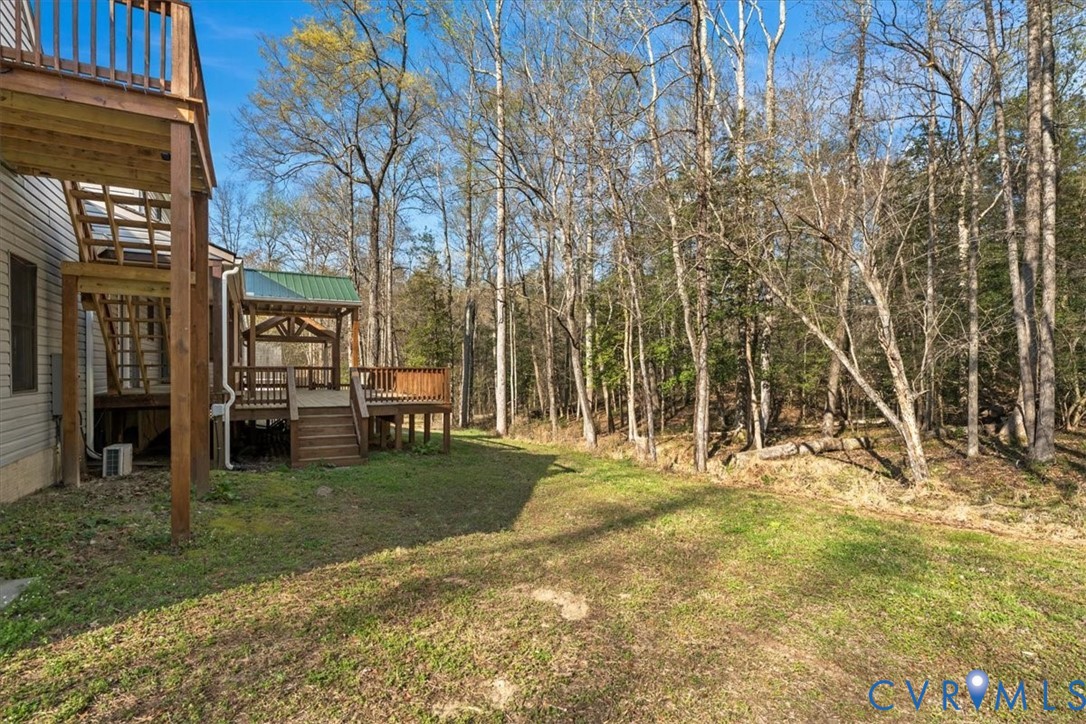 Multi-level wood deck with a metal roof accent, expansive rear grounds, and mature wooded tree line
