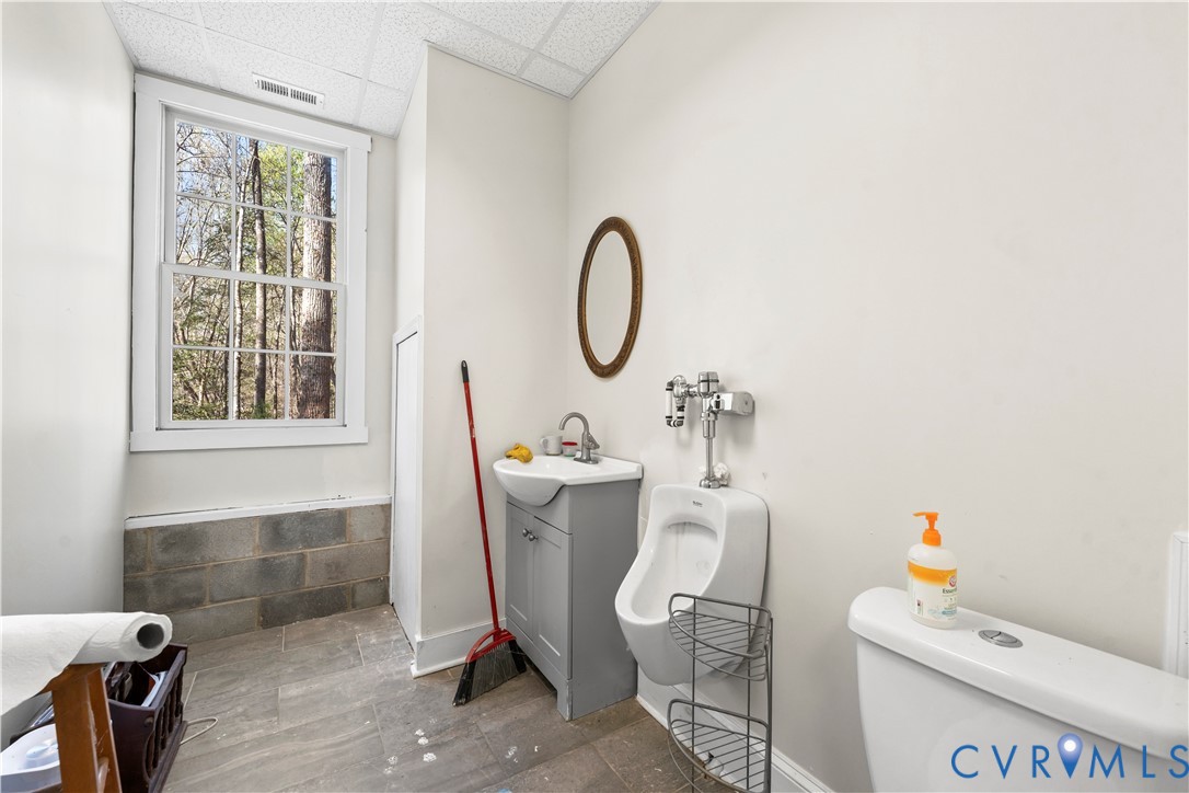 Single-hung window, grey vanity with a vessel sink, wall-mounted urinal, and tile flooring