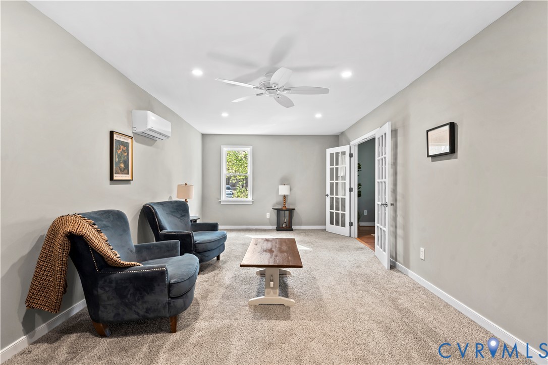 Interior space featuring wall-to-wall carpeting, recessed ceiling lighting, a ceiling fan, a wall-mounted ductless air conditioning unit, and white French doors Interior space featuring wall-to-wall carpeting, recessed ceiling lighting, a ceiling fan, a wall-mounted ductless air conditioning unit, and white French doors
