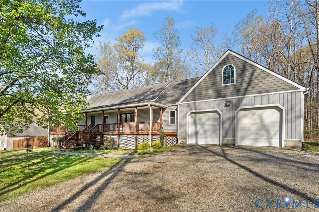Exterior featuring vertical and shingle siding, a covered wraparound wood porch, an attached two-car garage, and a semicircular arch window
