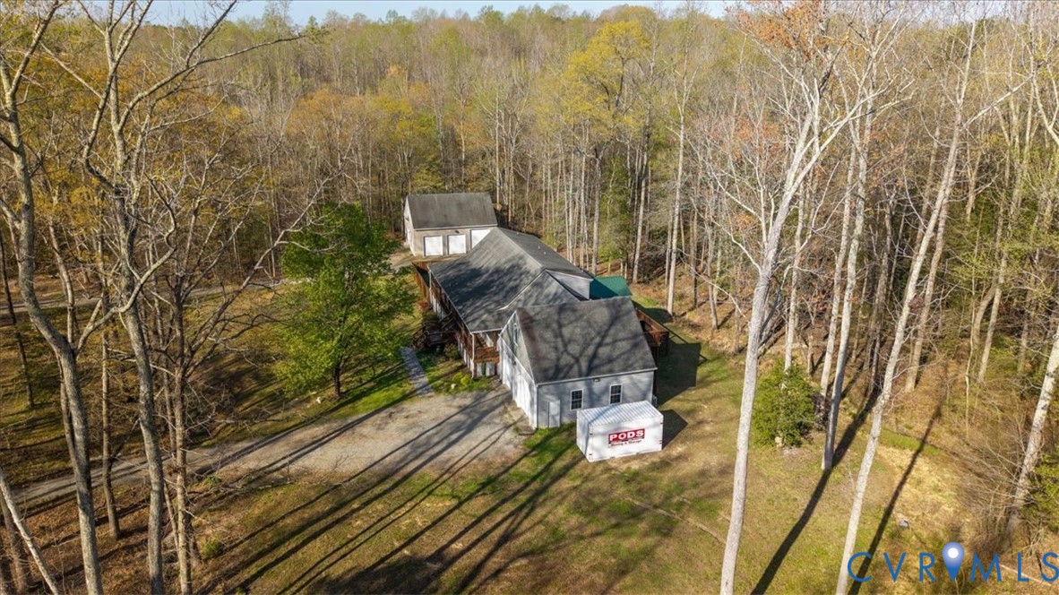 Residential structure featuring a pitched roof, attached garage, detached multi-bay garage, and extensive wooded grounds
