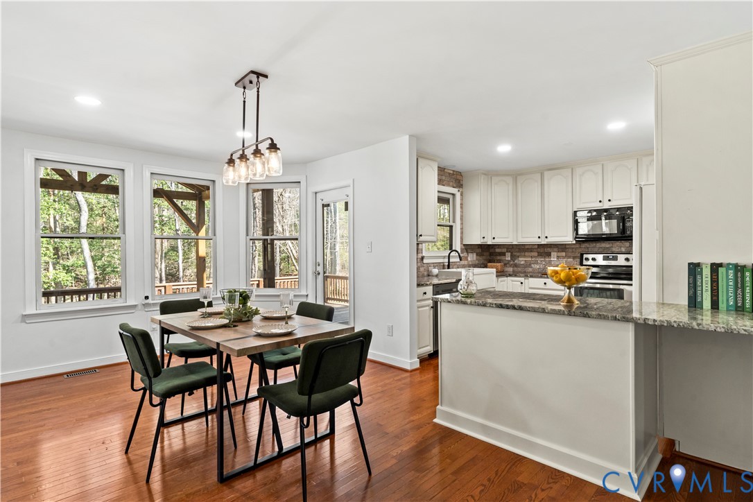 Kitchen featuring white cabinetry, stone countertops, a tile backsplash, and wood-finish flooring, complemented by a multi-light pendant fixture over the dining area