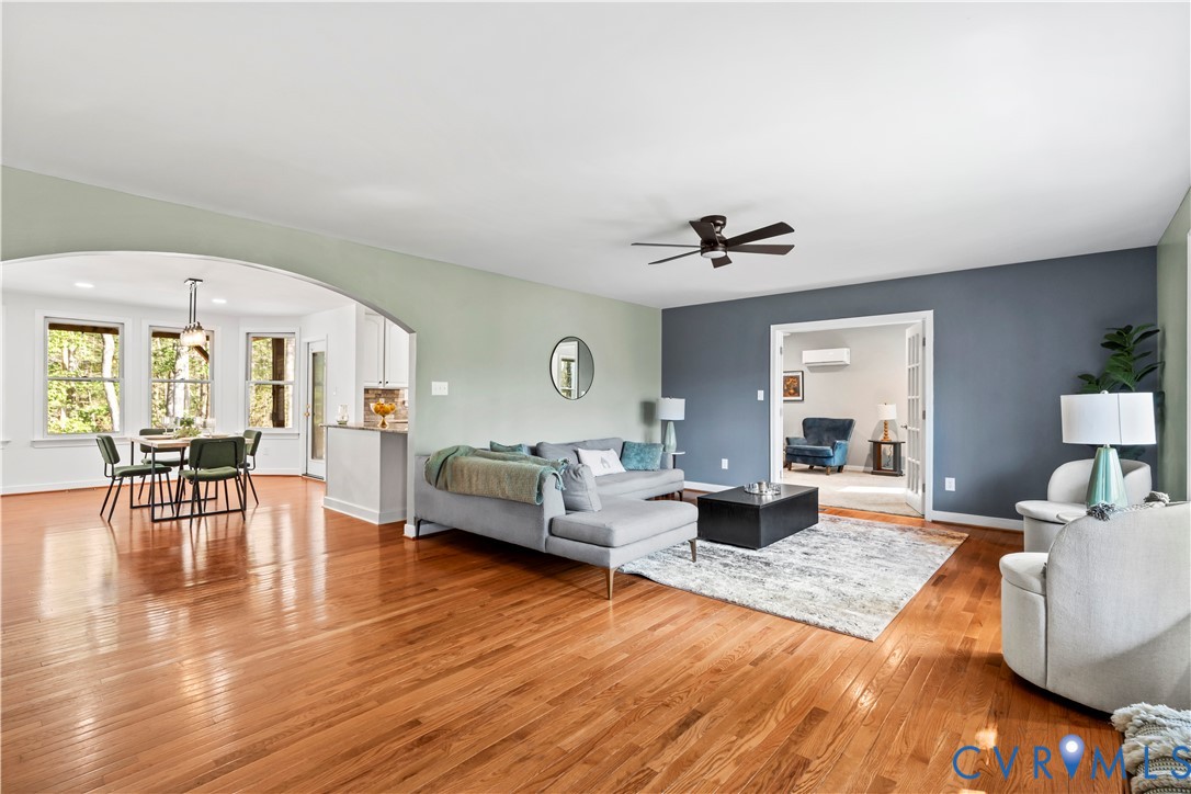 Open-concept interior featuring wood-finish flooring, a prominent arched architectural opening, multiple windows, a ceiling fan, and French doors Open-concept interior featuring wood-finish flooring, a prominent arched architectural opening, multiple windows, a ceiling fan, and French doors