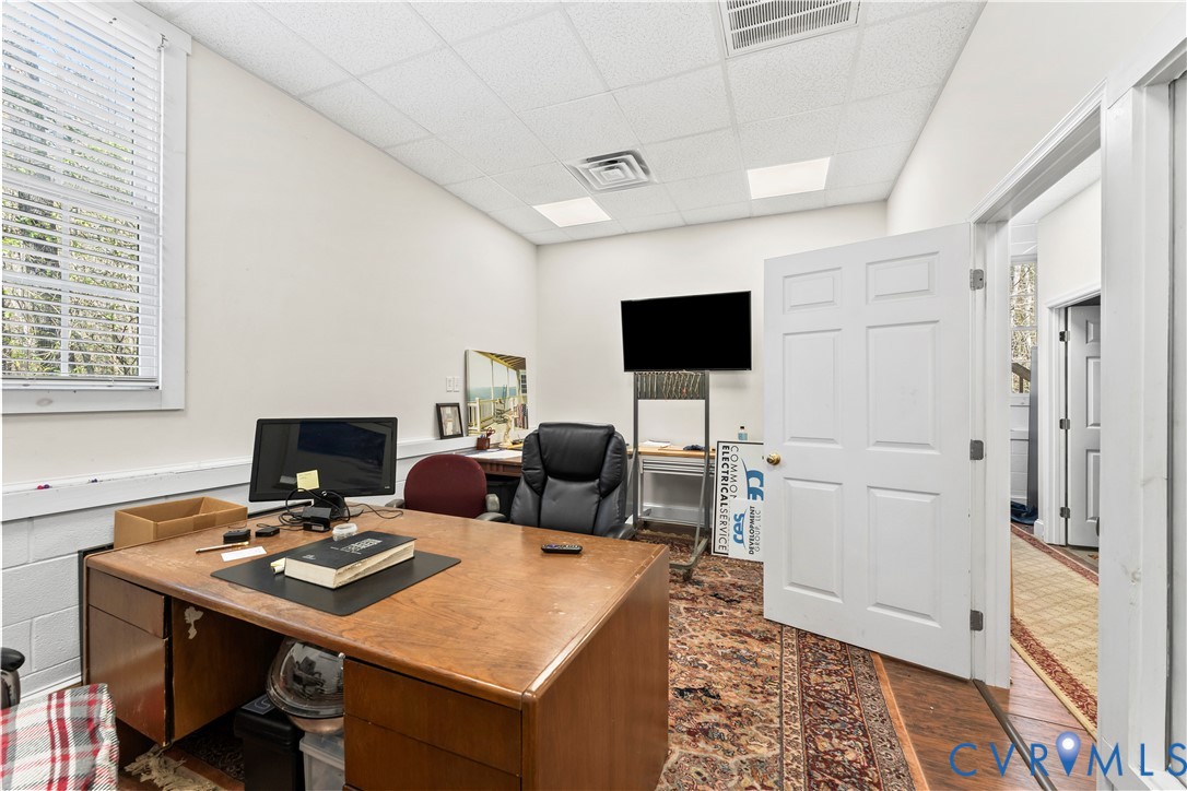 Room featuring a suspended acoustic tile ceiling, recessed panel door, and window with blinds