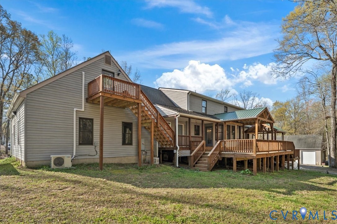 Multi-level exterior featuring light gray horizontal siding, a wrap-around wooden deck, a secondary-level balcony with stairs, and a metal-roofed covered patio area