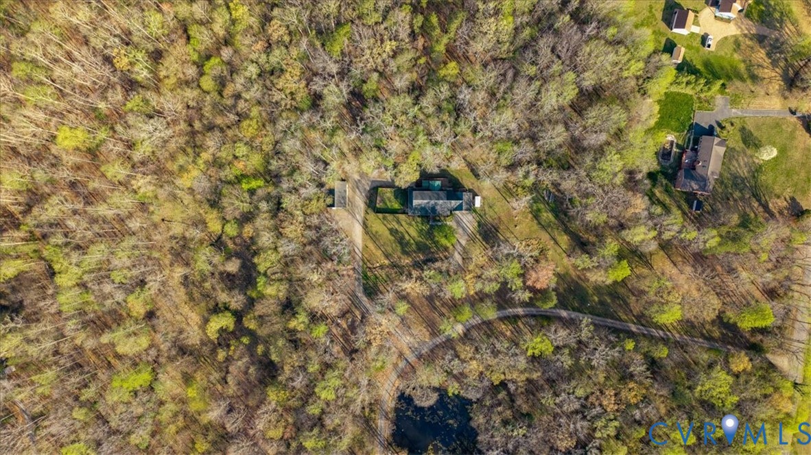 Aerial perspective of a multi-structure property featuring dense perimeter woodland, a paved driveway, and an expansive parcel