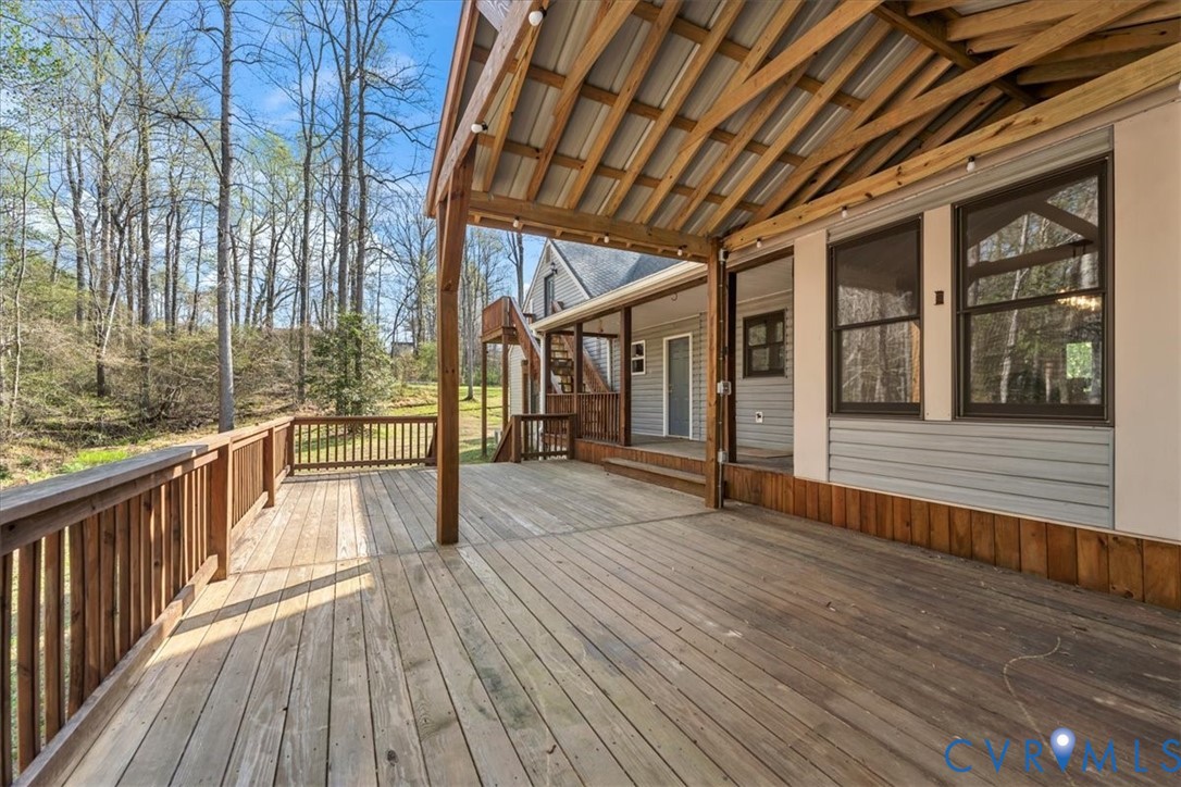 Expansive wooden deck featuring a covered area with exposed timber framing, horizontal siding, and a wooden perimeter railing