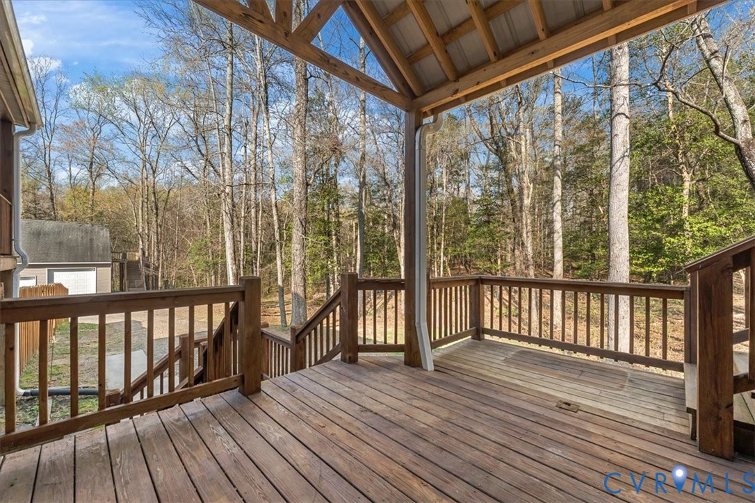 Covered wooden deck featuring an exposed truss ceiling, perimeter wood railings, and stairs leading to the ground level