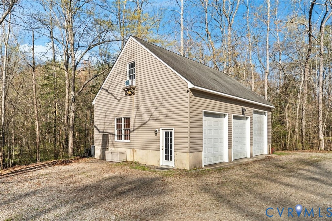Detached structure featuring three garage bays, vinyl siding, a concrete foundation, and an exterior pedestrian door