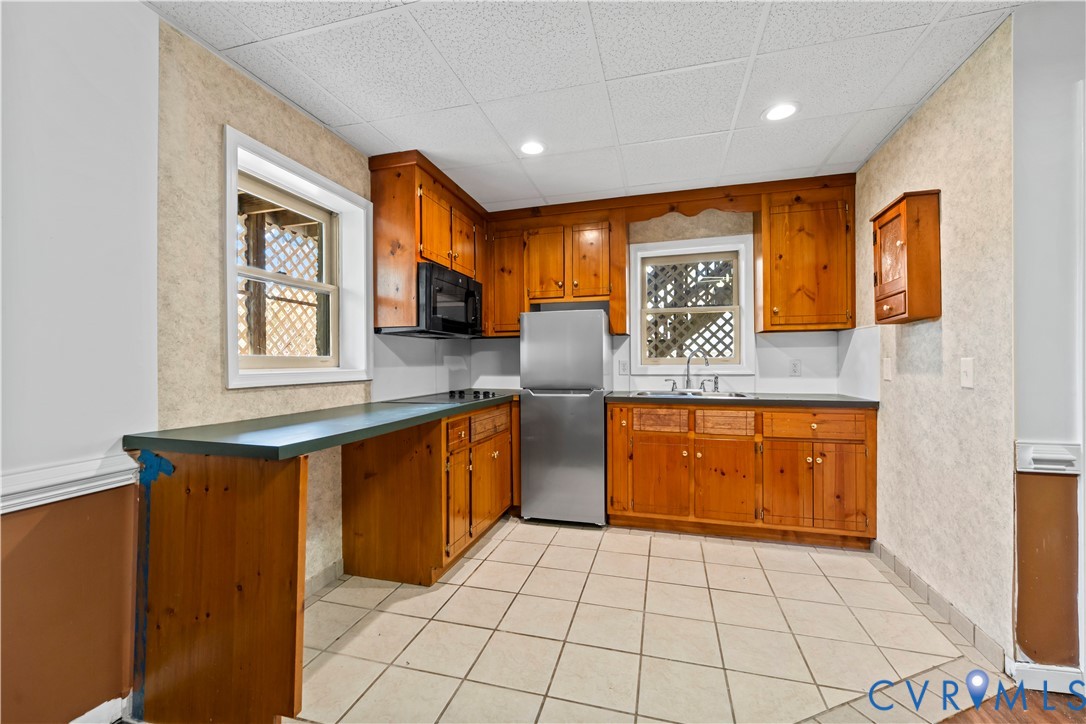 Kitchen featuring natural wood cabinetry, dark countertops, tile flooring, recessed lighting, and stainless steel refrigerator