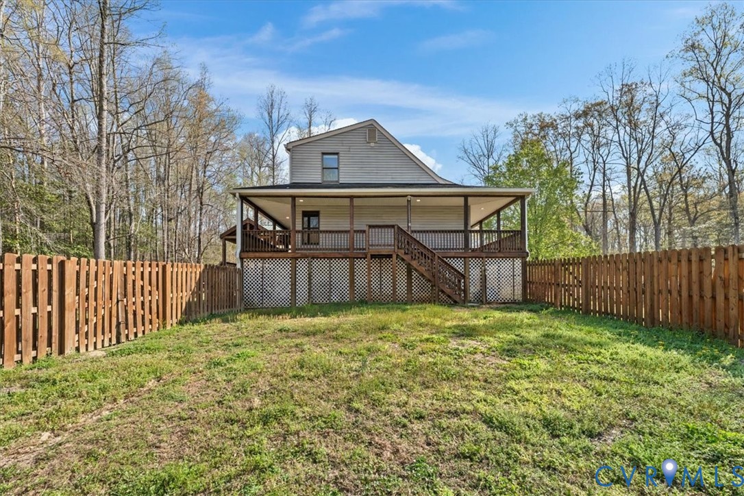 Exterior featuring a full-width covered deck with wooden railing and lattice skirting, enclosed by a wood privacy fence on a lot bordered by mature trees