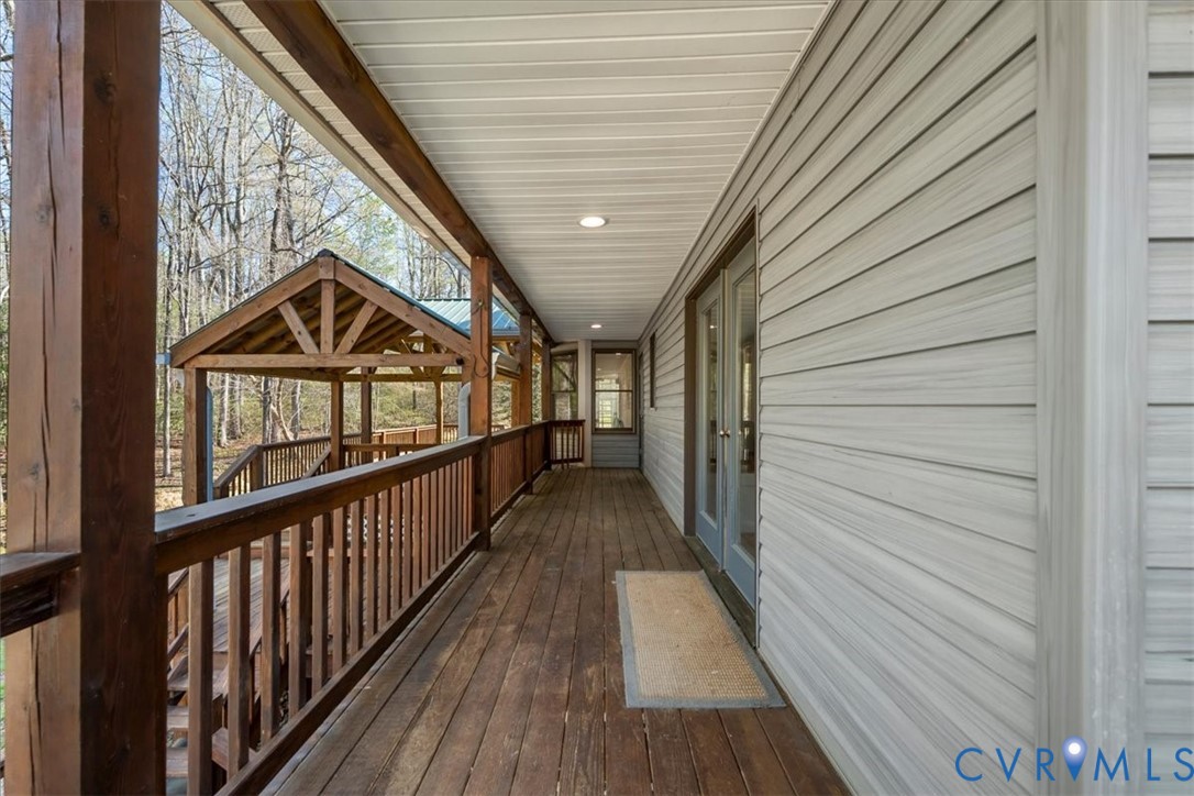 Covered exterior deck featuring wood-finish flooring, dark timber support posts, horizontal siding, and a wooden gazebo structure