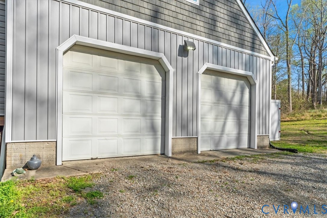 Two-car garage featuring vertical siding, shake-shingle gable, concrete foundation, and dual overhead doors