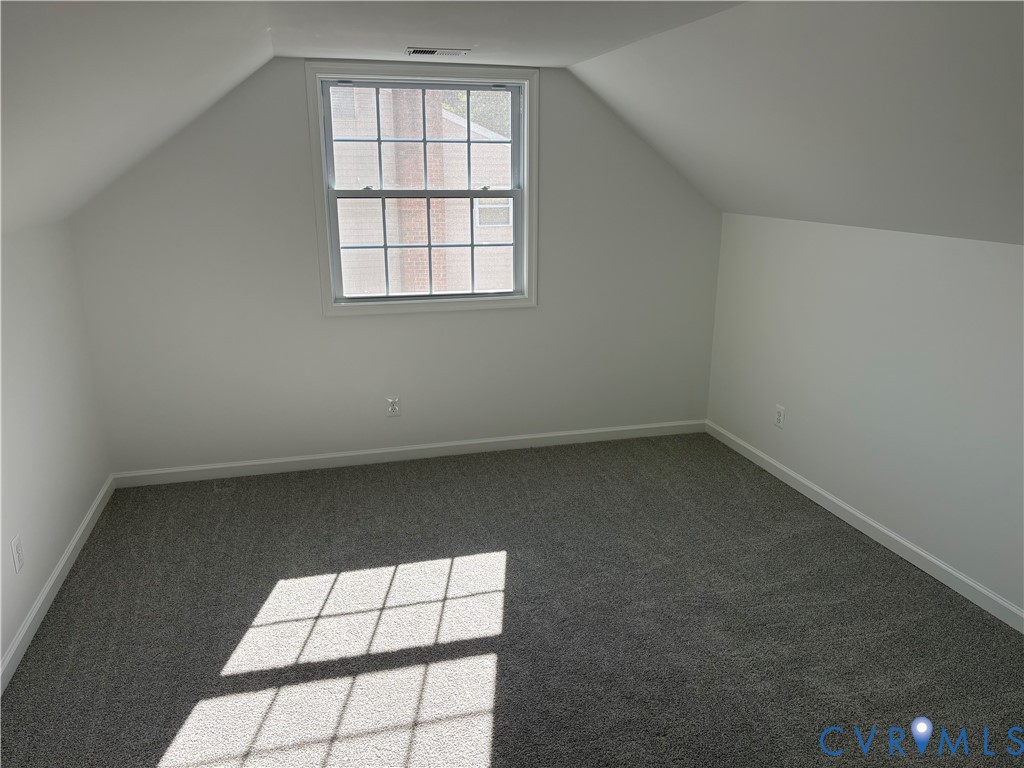Sloped ceilings, neutral wall color, grey wall-to-wall carpeting, and a multi-pane double-hung window