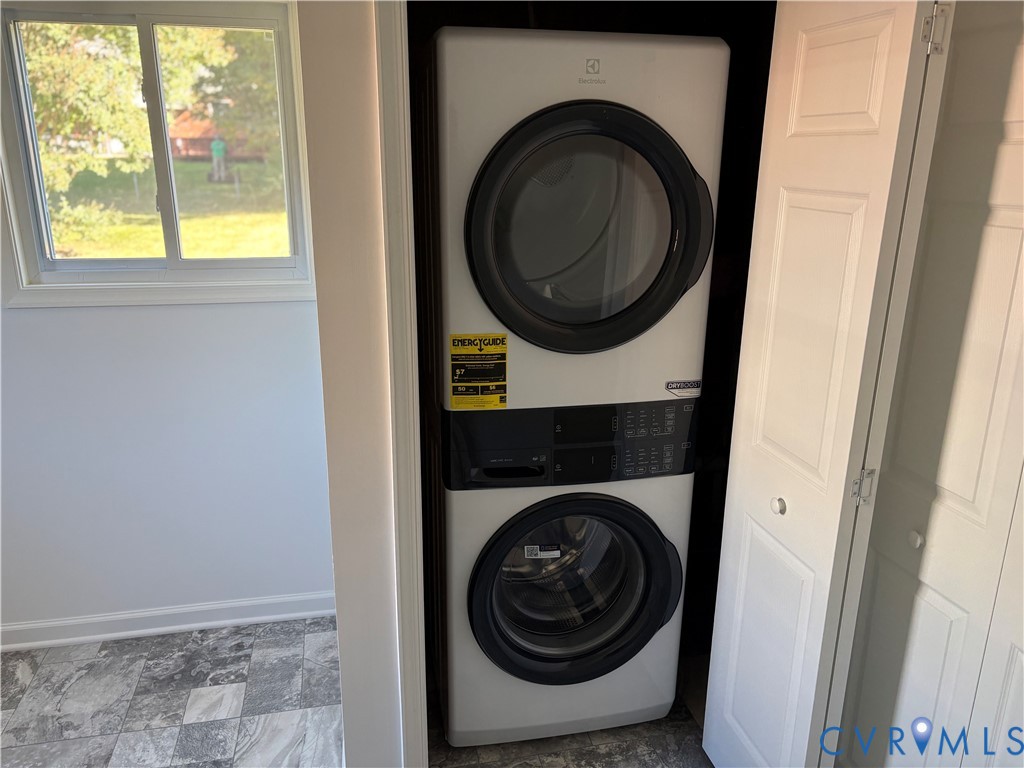 Stacked front-load laundry unit with digital controls, housed within a closet featuring white panel doors and set against stone-finish tile flooring