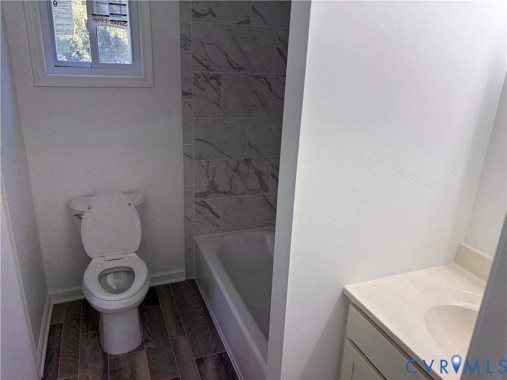 Bathroom 3rd level featuring a tub with stone-patterned tile surround, wood-finish flooring, a vanity with a solid-surface countertop, and a window