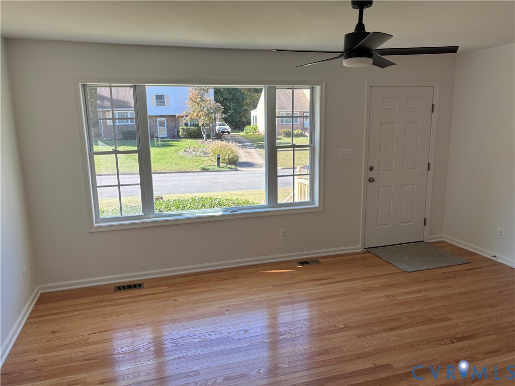 Living room featuring hardwood flooring, a large picture window, and a matte black ceiling fan
