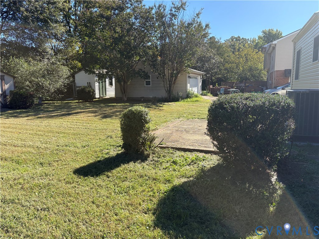 Expansive backyard featuring a grass lawn, mature trees, a concrete pad, and a detached garage