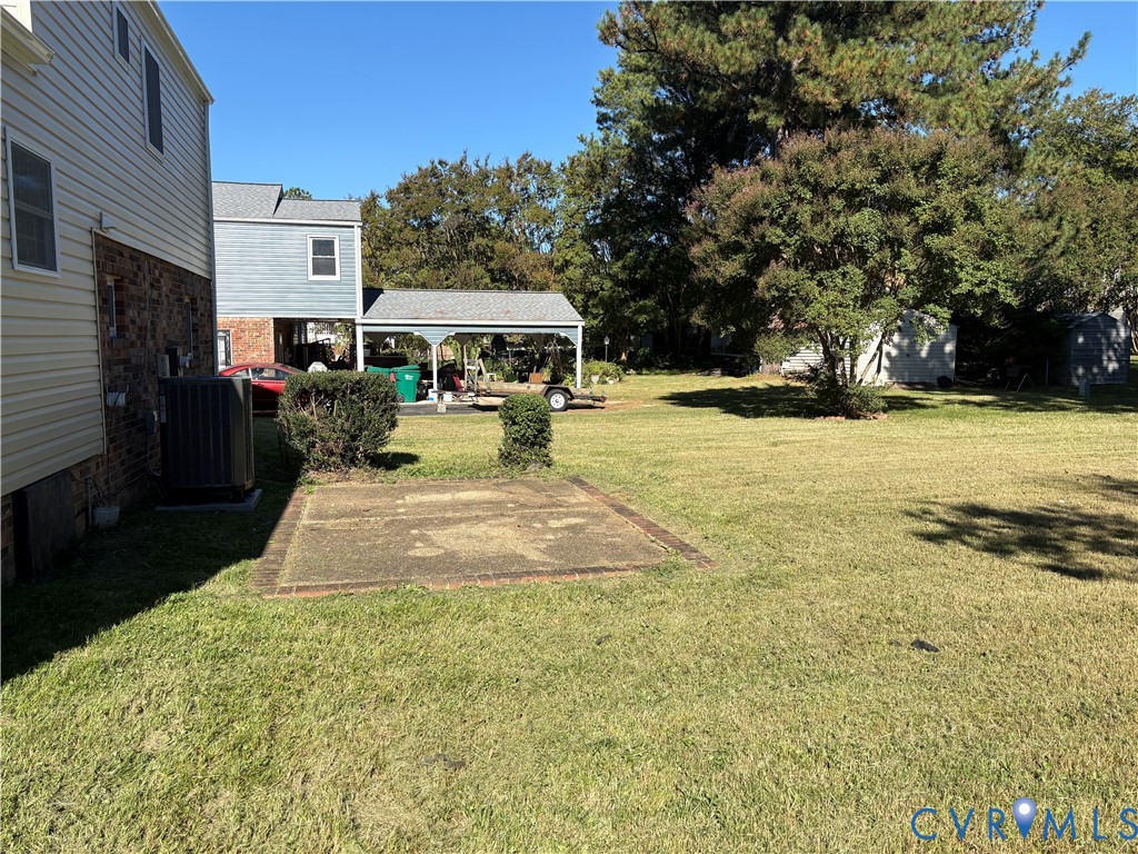 Exterior grounds featuring a concrete pad, a detached covered carport, mature trees, and partial brick and siding exterior