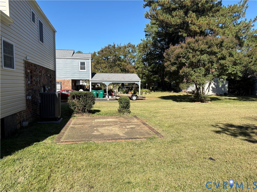 Expansive backyard featuring a concrete patio, covered parking structure, brick and siding exterior, and mature trees