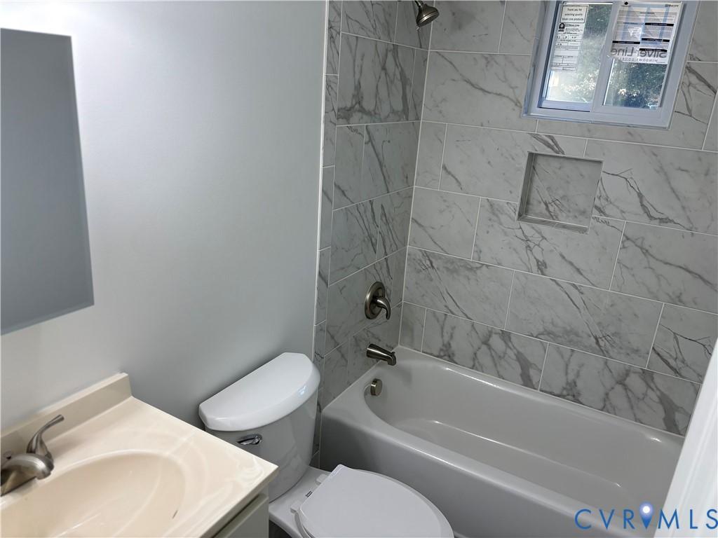 1st level Bathroom featuring a stone-look tile shower surround with a built-in recessed niche, tub-shower combination, vanity with an integrated sink, and metal finish fixtures