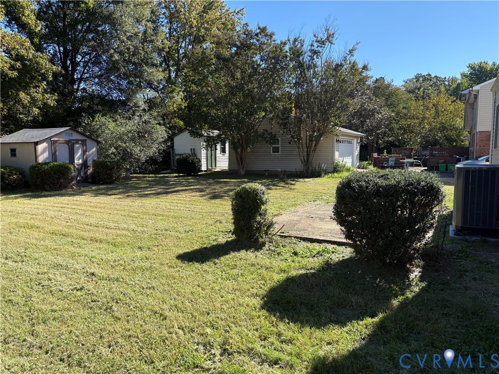 Expansive backyard featuring a manicured lawn, concrete patio area, two detached storage structures, and mature trees