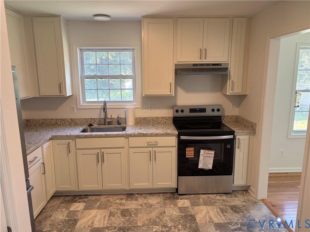 Kitchen featuring off-white shaker cabinetry, speckled stone-finish countertops, stainless steel appliances, a double-basin undermount sink, and tile flooring