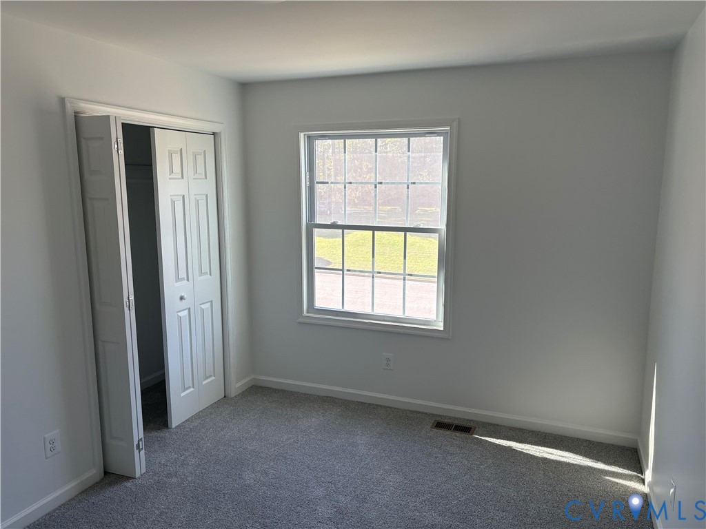 Bedroom 2 Neutral interior space featuring neutral wall paint, carpeted flooring, a grid-patterned window, and a white bifold closet door