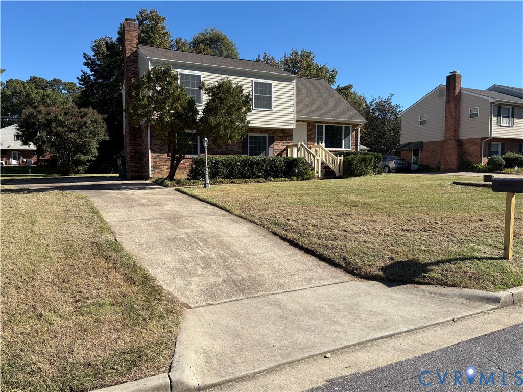 Split-level exterior featuring a brick and horizontal siding facade, a side-gable roofline, a prominent exterior chimney, and a concrete driveway Split-level exterior featuring a brick and horizontal siding facade, a side-gable roofline, a prominent exterior chimney, and a concrete driveway