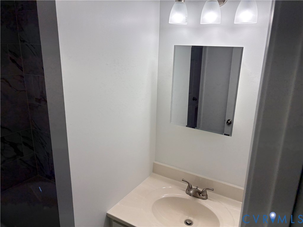 Bathroom 3rd level featuring a vanity with integrated sink, chrome double-handle faucet, wall-mounted mirror, three-light fixture, and tile shower surround