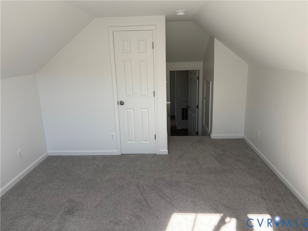 Finished attic space featuring vaulted ceilings, neutral carpeting, a six-panel interior door, and built-in access panel