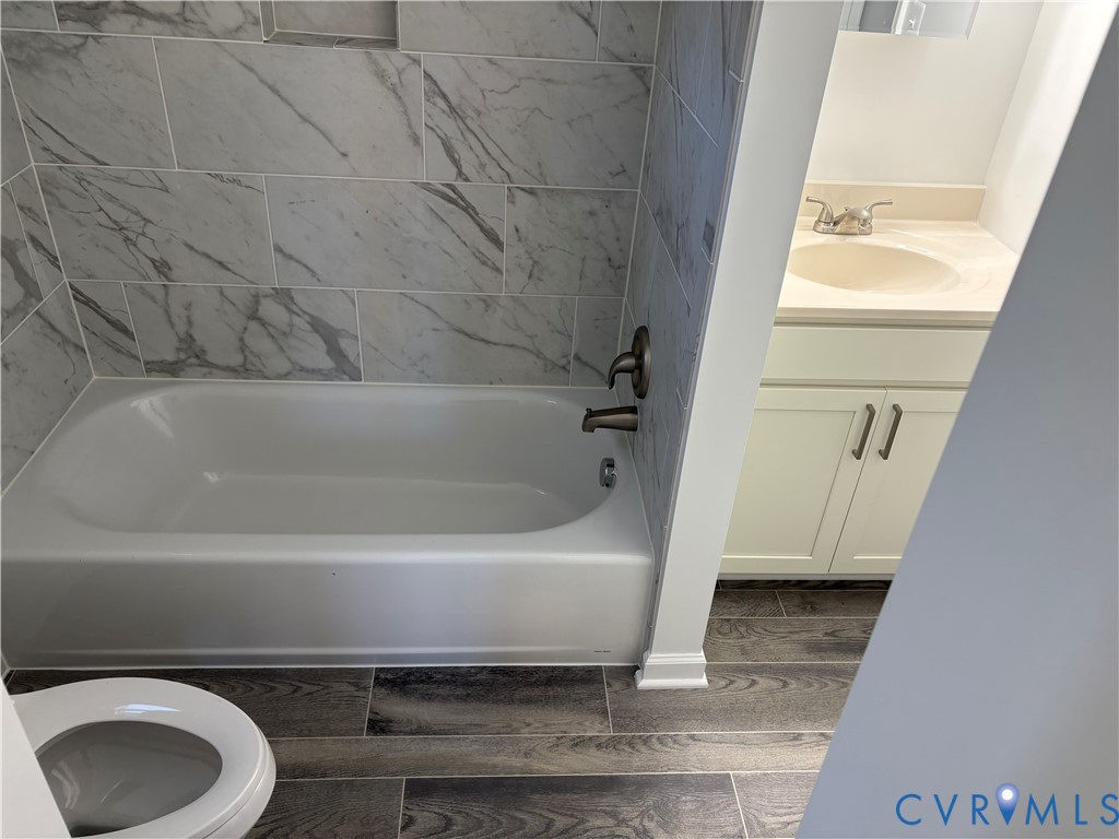 Bathroom 3rd level featuring a tub-shower combination with floor-to-ceiling large-format stone-patterned tile, wood-finish flooring, white cabinetry with metallic hardware, and an integrated countertop sink