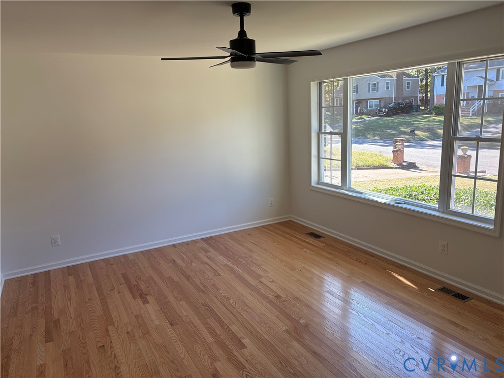 Living room featuring wood-finish flooring, a large multi-pane window, and a matte black ceiling fan