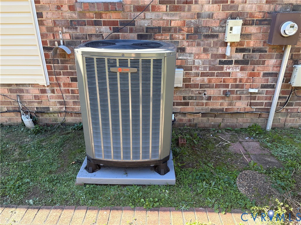 Trane central air conditioning unit mounted on a concrete slab against a red brick exterior