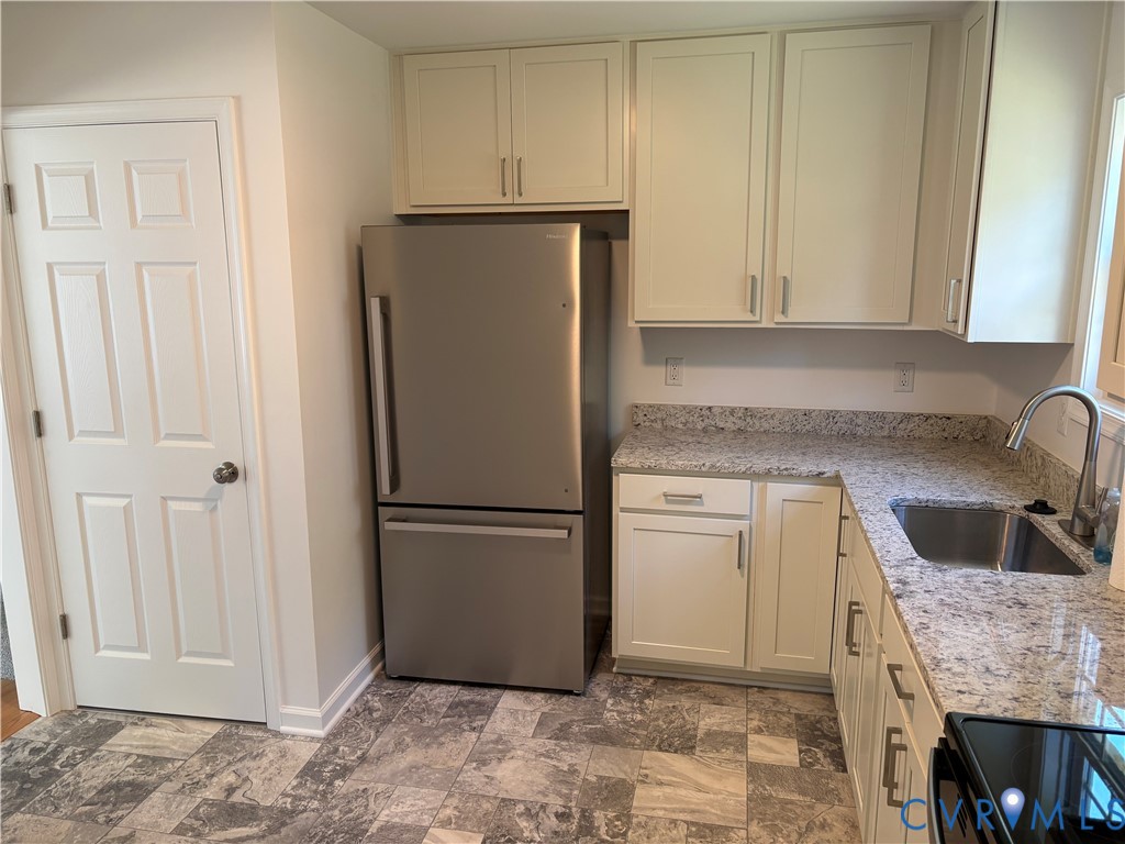 Kitchen featuring light-toned shaker cabinetry, stone-finish countertops, stainless steel undermount sink with arched pull-down faucet, stainless steel bottom-freezer refrigerator, and multi-tone tile flooring